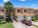 Townhome exterior featuring a well-manicured lawn, brick driveway, attached garage, and a vibrant palm tree at 1434 Pacific Rd, Kissimmee, FL 34759