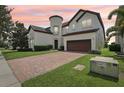 Charming two-story stucco home featuring a tile roof, brick driveway, and manicured lawn at sunset at 9207 Busaco Park Way, Winter Garden, FL 34787