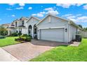View of a well-kept one-story home with a two-car garage, lovely landscaping, and a brick-paved driveway at 1061 Castlevecchio Loop, Orlando, FL 32825