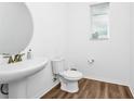 Simple half bathroom with white fixtures, wood-look floor and circular mirror above the sink at 812 Benoi Dr, Davenport, FL 33896