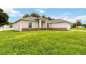 A view of the side and front of this single-story home, showing a brick foundation and lush lawn at 630 Park Valley Cir, Minneola, FL 34715