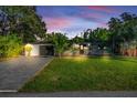 Beautiful home exterior at dusk with lush green lawn, long driveway, and tasteful landscaping with tropical plants at 6805 Barby Ln, Belle Isle, FL 32812