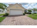 Inviting home exterior featuring a two-car garage and a brick driveway, surrounded by lush greenery and landscaping at 3585 Ventura Club Cir, Orlando, FL 32822