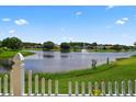 Scenic lake view featuring a fountain, lush greenery and a partial white picket fence at 2076 Shannon Lakes Blvd, Kissimmee, FL 34743