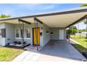 View of a convenient covered carport with a yellow front door and gray siding, and manicured landscaping at 3515 Leslie Dr, Orlando, FL 32806