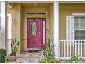 Close-up of a red front door, side panel window, white porch railing and cream colored exterior at 7939 Riffle Ln, Orlando, FL 32818