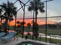 Relaxing screened-in pool area with beautiful sunset views, palm trees, and outdoor lounge seating at 448 Warrior Trl, Deltona, FL 32725