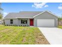 Well-maintained single-story home with a two-car garage, a red front door, and fresh landscaping at 654 Ne 130Th Ct, Silver Springs, FL 34488