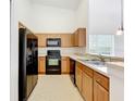 Galley kitchen with wood cabinets, black appliances, and tile flooring at 2092 Switch Grass Cir, Ocoee, FL 34761