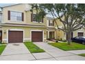 Beautiful townhome featuring a brown two-car garage, tan exterior paint, green grass, and an airy tree at 1967 Beacon Bay Ct, Apopka, FL 32712