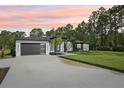 Modern home with a spacious driveway and manicured lawn, set against a backdrop of lush trees at sunset at 42157 Tamarac St, Eustis, FL 32736