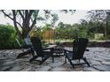 An outdoor stone patio with a fire pit and three black chairs surrounded by lush greenery and a wooden fence at 610 Cypress Ave, Orange City, FL 32763