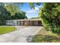 A single-story home with a brick facade, covered parking, a long driveway, and mature trees at 622 Avenue D Se, Winter Haven, FL 33880