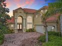 Exterior view of a tan two-story home with a red brick driveway and tropical landscaping at sunset at 2209 Callaway Ct, Davenport, FL 33837