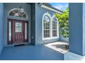 Inviting entryway showcasing a detailed wood door, arched windows, modern lighting, and well-kept landscaping at 1031 Seneca Trl, St Cloud, FL 34772
