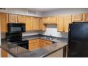 A kitchen with wood cabinets, dark grey countertops, and black appliances provides a functional cooking space at 420 Forestway Cir # 202, Altamonte Springs, FL 32701