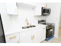 Modern kitchen featuring white cabinetry, gold hardware, stainless steel appliances, and a tile backsplash at 4469 Evers Pl, Orlando, FL 32811