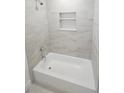 Bright bathroom with white tub, tiled walls, and recessed shelving for storage at 311 Osceola Ave, Lake Wales, FL 33853