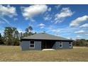 The backyard of a contemporary house featuring dark gray stucco walls, a gray shingled roof, and a spacious lawn at 4062 Sw 114Th St, Ocala, FL 34476