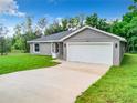 Charming single-story home features a gray exterior, a spacious two-car garage, and a long driveway at 24780 Nw Hillsdale Ave, Dunnellon, FL 34431