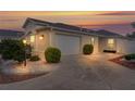 Exterior view of a single story home with a two car garage and manicured front yard at sunset at 1673 Belle Grove Dr, The Villages, FL 32162