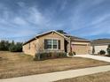 Tan house with stone accents, two-car garage, and landscaped yard at 6365 Sw 88Th Loop, Ocala, FL 34476