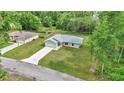 Aerial shot of a light-gray home with attached garage, a long driveway, and green lawn in a wooded area at 963 Nw 65Th St, Ocala, FL 34475