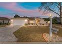 Charming one-story home featuring an attached garage, beautiful landscaping, and inviting front entrance at dusk at 9910 Se 138Th Loop, Summerfield, FL 34491
