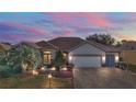 Inviting single-story home with manicured landscaping, paver driveway, and an attached two-car garage at dusk at 13077 Se 86 Ct, Summerfield, FL 34491