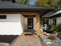 Inviting front entrance featuring a brick walkway, modern black door, wood accents, and beautiful garden features at 13061 Se 158Th Ln, Weirsdale, FL 32195