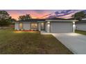 Inviting single-story home featuring a two-car garage and manicured lawn with colorful sunset at 13910 Sw 113 Ln, Dunnellon, FL 34432