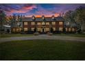 Stately two-story brick home featuring a circular driveway, manicured lawn and mature trees, warmly lit at twilight at 4940 E Fort King St, Ocala, FL 34470
