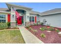 Lovely landscaped front yard with red accents including a red front door and shutters, as well as an American flag at 1083 Se 65Th Cir, Ocala, FL 34472