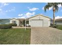 Inviting one-story home showcases a brick-paved driveway and lush green lawn complemented by a mature palm tree at 2538 Privada Dr, The Villages, FL 32162