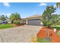 Home exterior featuring a two-car garage, paver driveway, and mature trees on a sunny day at 10138 Lake Miona Way, Oxford, FL 34484