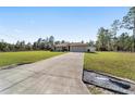 Spacious single-story home featuring a lengthy driveway, two-car garage, and expansive green lawn at 4826 Sw Dahlia Ct, Dunnellon, FL 34431