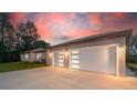 Spacious three-car garage with modern doors and ample parking space, complemented by a lovely sunset backdrop at 4869 Nw 101St Street Rd, Ocala, FL 34482