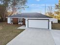 Modern one-story home featuring a large driveway and a two-car garage, set against a clear blue sky at 13384 Sw 105 Pl, Dunnellon, FL 34432