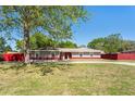 Single-story home featuring a red fence, well-maintained lawn, and large tree providing shade at 5041 Ne 4Th St, Ocala, FL 34470