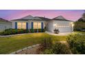 Charming home with a manicured lawn, blue shutters, and a two-car garage at twilight at 1854 Oxford Lane, The Villages, FL 32162