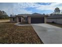 Tan, one-story home with a dark garage door and a long driveway at 13 Locust Trak, Ocala, FL 34472