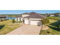Aerial view of a single-story home with a well-manicured lawn, paver driveway, and lake view at 6558 Sw 94Th Cir, Ocala, FL 34481