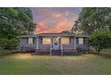 Cozy single-story home with a welcoming front porch, featuring green shutters and lush landscaping at sunset at 2720 Se 145Th St, Summerfield, FL 34491