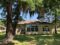 Back of a tan house with a sunroom, visible through large trees with hanging Spanish moss at 10918 Sw 71St Cir, Ocala, FL 34476
