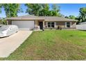 Single-story home featuring an attached garage, well-kept lawn, and a car covered with a silver protector at 4243 Se 131St Ln, Belleview, FL 34420
