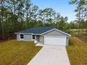 Inviting single-story home showcasing a gray exterior, attached garage, concrete driveway and naturally landscaped front yard at 24354 Nw Water Oak Ave, Dunnellon, FL 34431