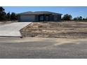 A single-story home with a gray exterior, concrete driveway, a front yard covered with sand, and a blue sky at 4424 Sw Carnation Ct, Dunnellon, FL 34431