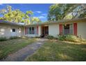 Inviting home entrance featuring red shutters and door, complemented by well-kept front lawn and walkway at 16571 Se 95Th Street Rd, Ocklawaha, FL 32179