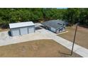 Aerial view of a gray home with attached carport and detached three-car garage with concrete driveway at 9885 Se 144Th St, Summerfield, FL 34491