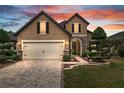Charming two-story home featuring a brick driveway, manicured lawn, and stone accents on the facade at sunset at 6816 Sw 95Th Cir, Ocala, FL 34481